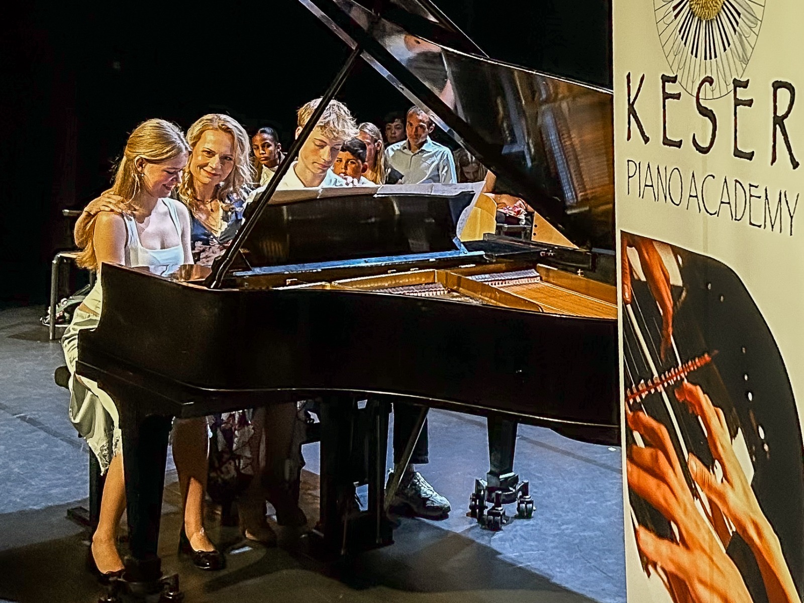 Hülya Keser with students around a grand piano at a Keser Piano Academy performance