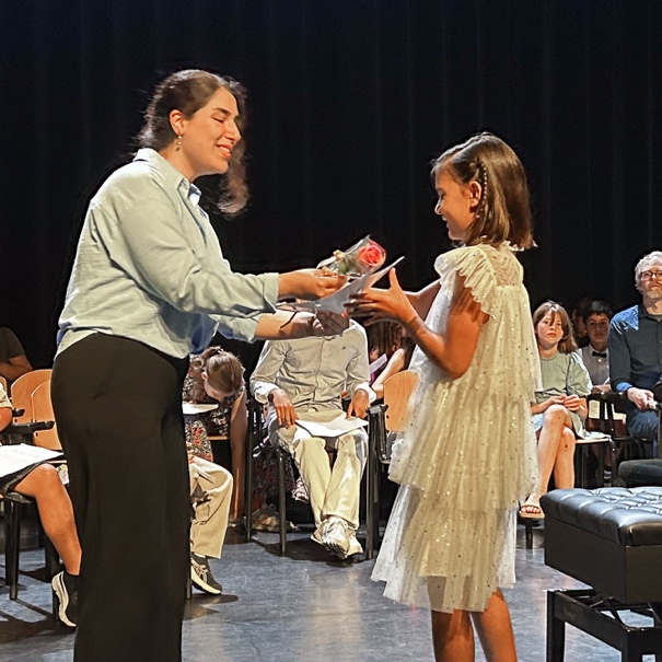 A woman handing a flower and a certificate to a young girl on stage