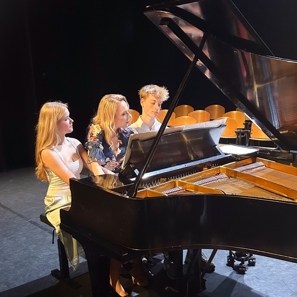 Three people sitting at a grand piano on stage